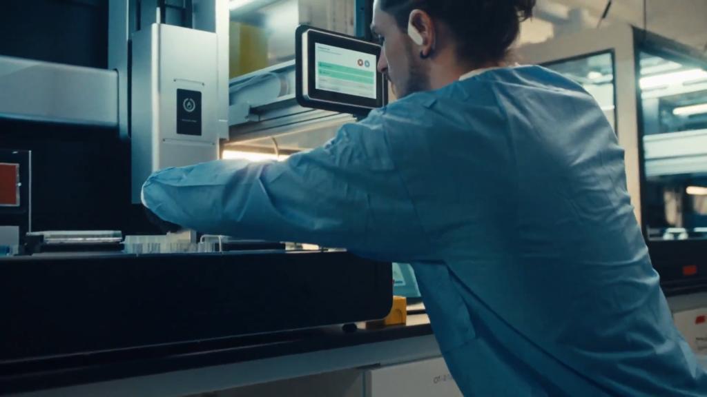 A scientist in a blue coat interacting with an AI-programmed Opentrons robot in a lab at Opentrons headquarters in Long Island City